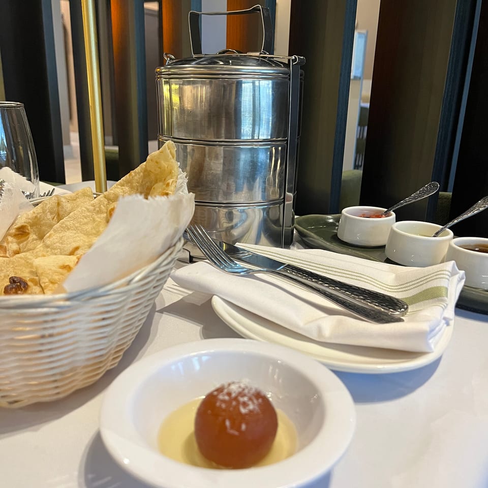 Restaurant table set with crisp bread, sauces, stacked metal serving dishes, and a round dessert in syrup.