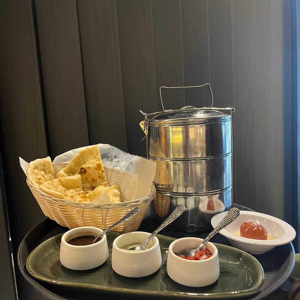 Restaurant buffet featuring a basket of crisp flatbreads, serving dishes of sauces, a dessert, and stacked stainless-steel containers.
