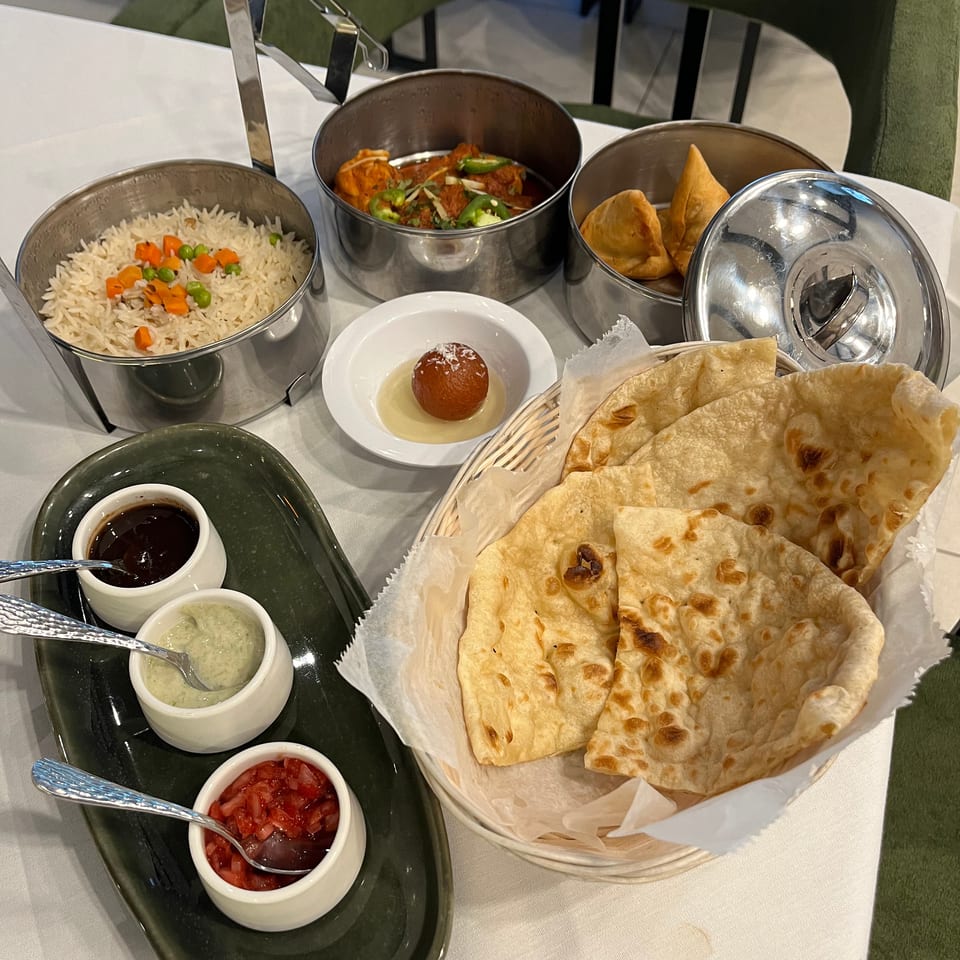 Indian meal spread with naan, vegetable rice, curry, samosas, chutneys, and dessert arranged on a restaurant table.