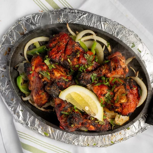 Sizzling tandoori chicken with onions, green peppers, and a lemon wedge in a cast iron skillet.