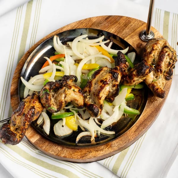 Grilled chicken skewers with charred edges, served on a sizzling platter with sautéed onions and peppers.