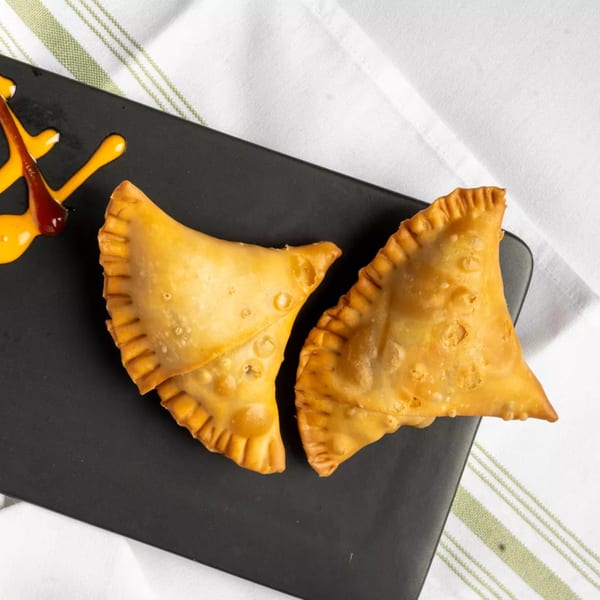 Two golden-brown empanadas with crimped edges on a black plate with orange and red sauce.