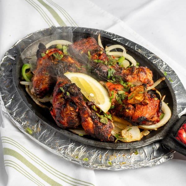 Sizzling tandoori chicken with onions, green peppers, and cilantro, garnished with a lemon wedge.