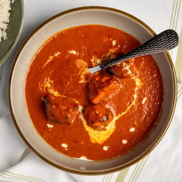Overhead view of a bowl of chicken tikka masala with a spoon and a side of rice.