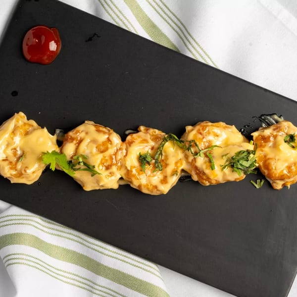 Five pieces of fried shrimp covered in creamy sauce and cilantro, with a dollop of red sauce.