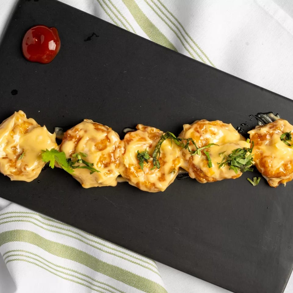 Five pieces of fried shrimp covered in creamy sauce and cilantro, with a dollop of red sauce.