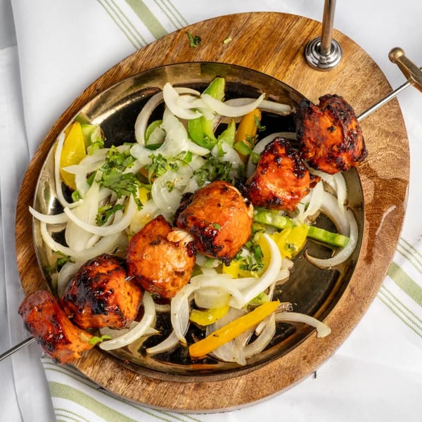 Tandoori chicken tikka skewers with charred edges, served on a bed of sliced onions and peppers.